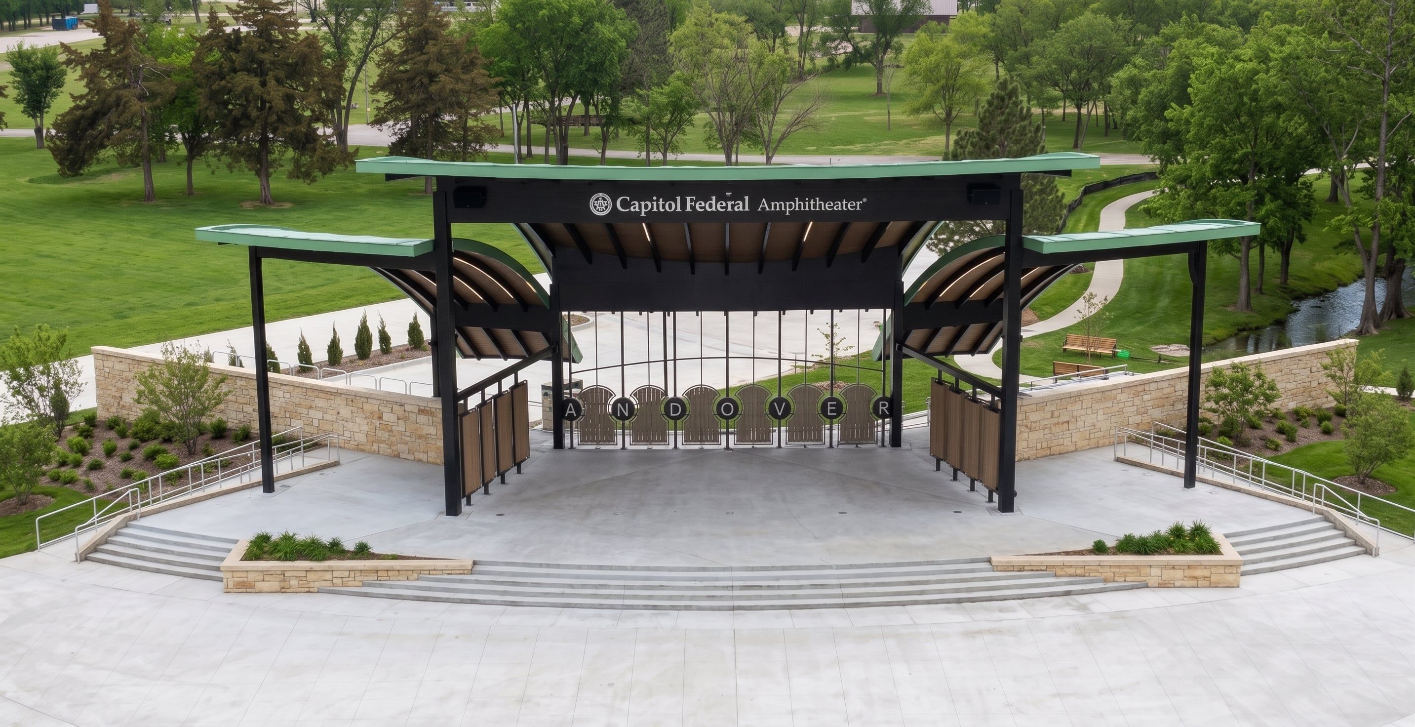 An aerial view of Capitol Federal Amphitheater surrounded by the open lawns, walking paths, and a stream of Andover Central Park