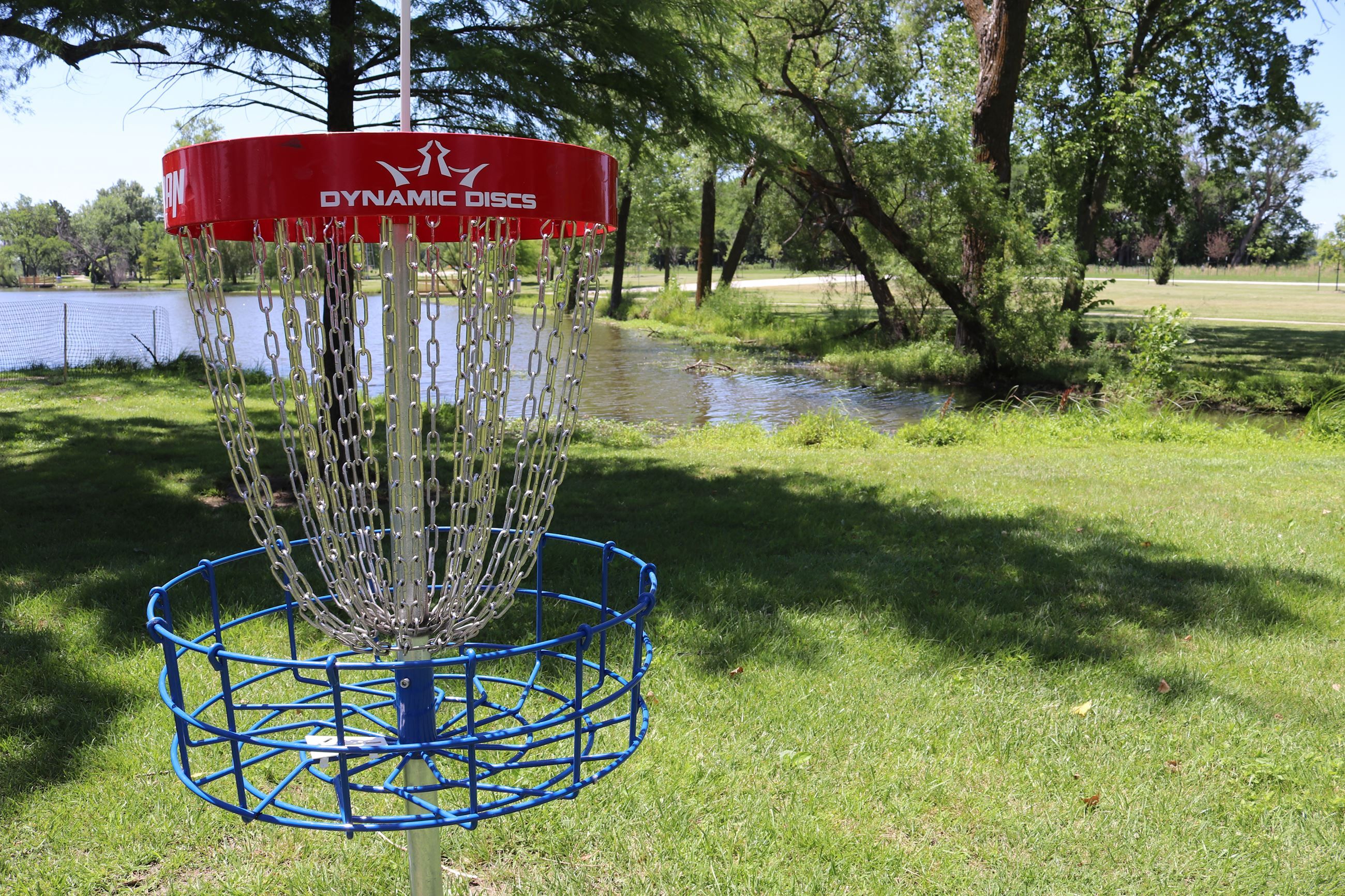 A disc golf basket beside the pond at Andover Central Park