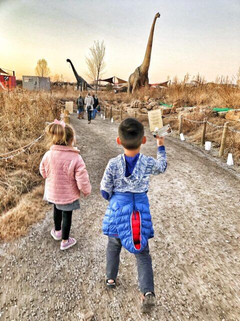 Two children walking a gravel trail toward large dinosaur models at Field Station: Dinosaurs