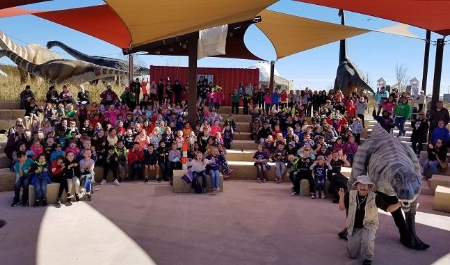 A large group of schoolchildren watching a costumed dinosaur presentation at Field Station: Dinosaurs