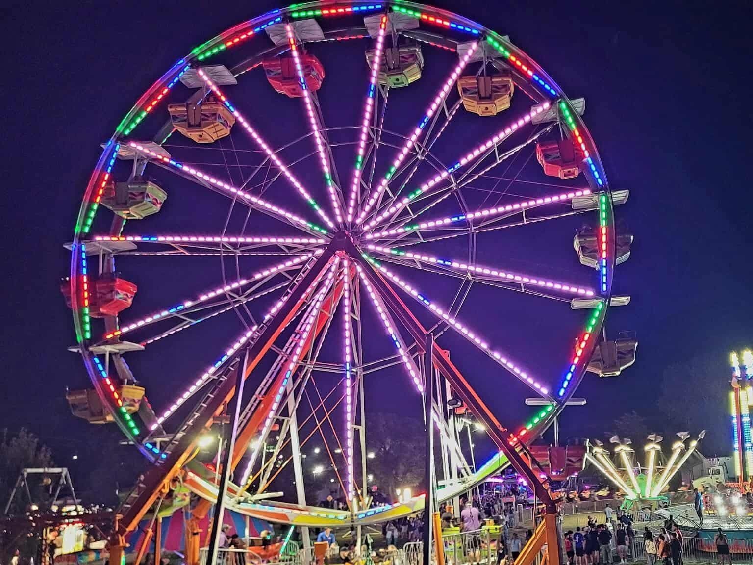 An illuminated Ferris wheel and carnival rides against the night sky at the Goddard Fall Festival