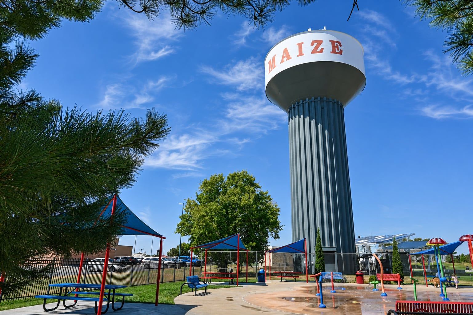 The Maize water tower rising above the splash pad and shaded picnic tables at Maize City Park