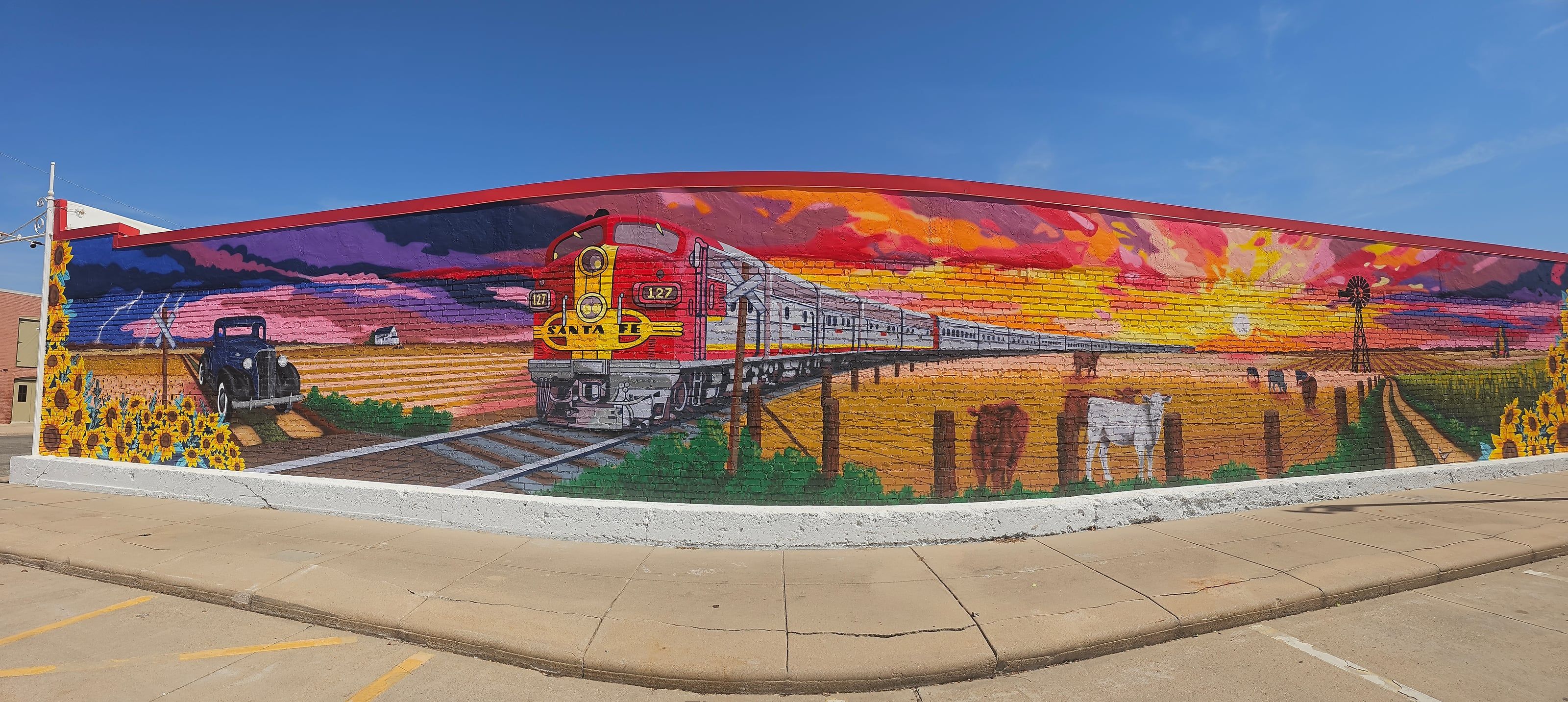 The Enz Auto Glass mural at 127 E 6th Street in Newton, depicting a 1937 Chevy, the Santa Fe Super Chief train, cattle, a windmill, and a sunflower field at sunset