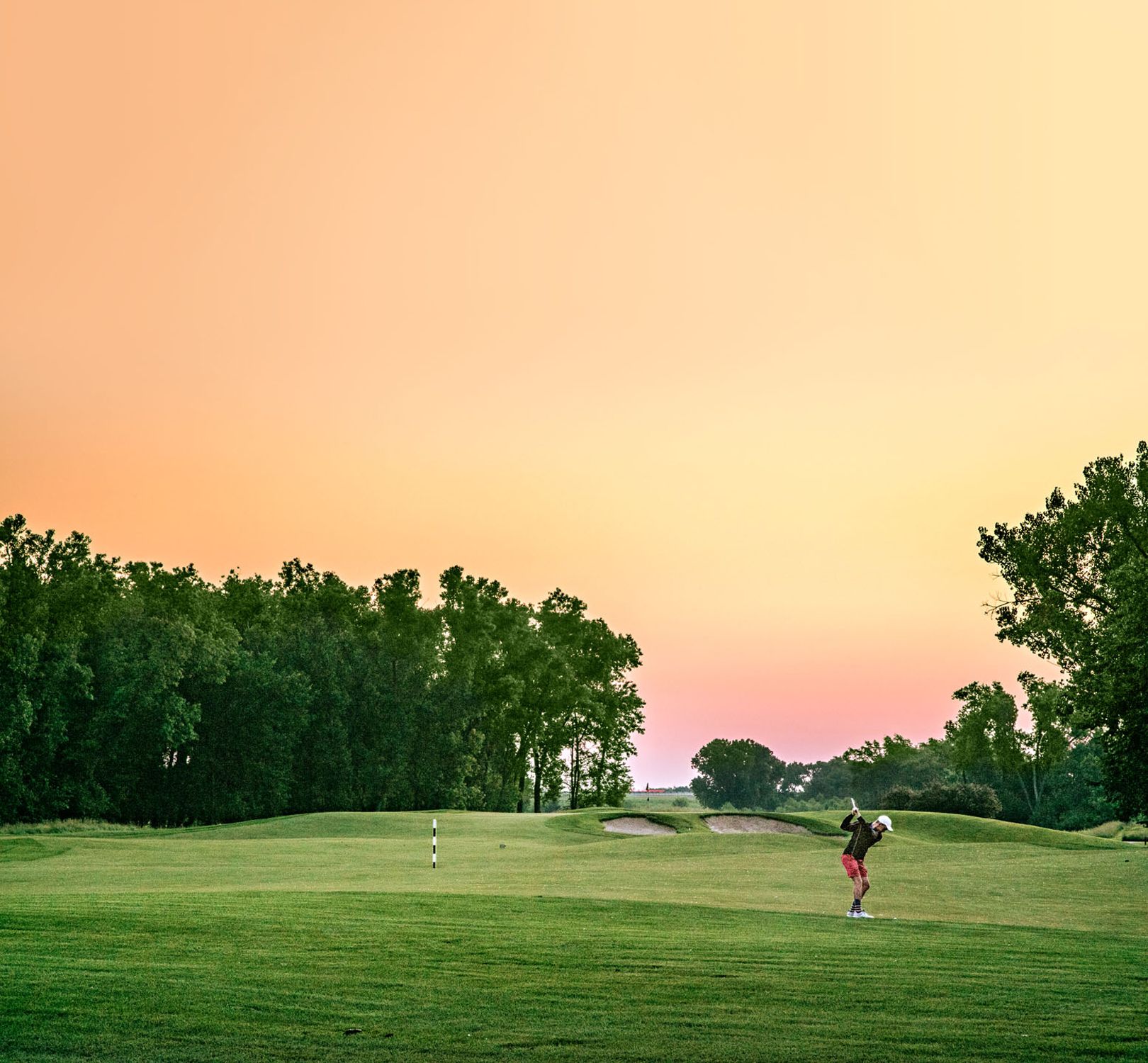 A golfer finishing a swing on the green at Sand Creek Station Golf Course in Newton at sunset