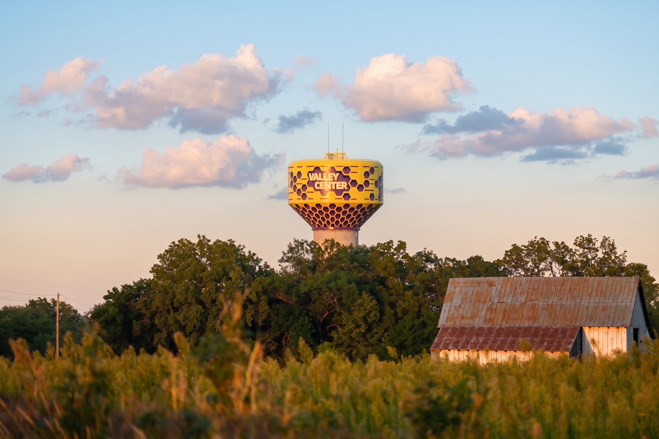 The Valley Center water tower at golden hour, rising above a tree line with a weathered barn in the foreground