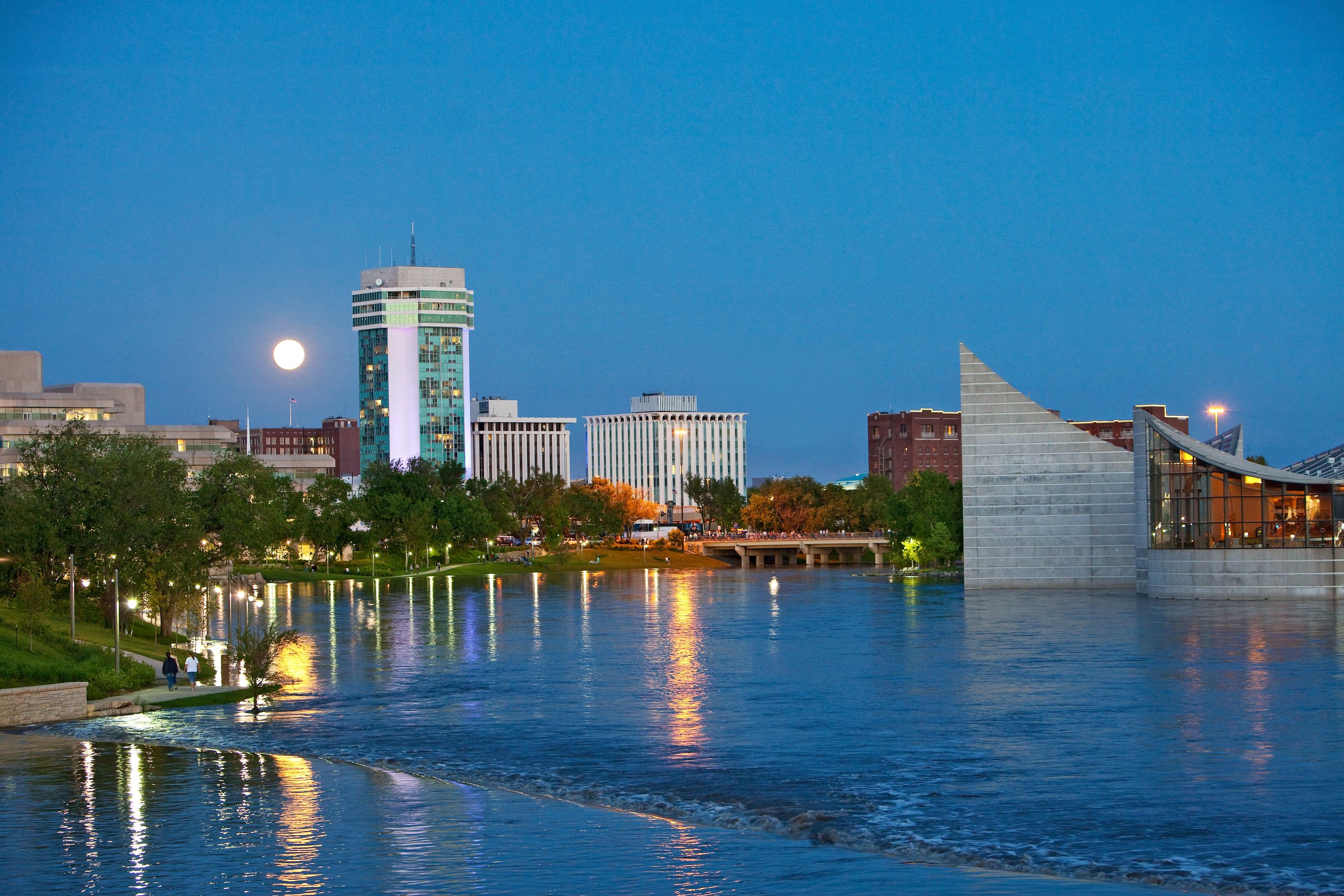 The downtown Wichita skyline reflected in the Arkansas River at dusk, with a full moon rising
