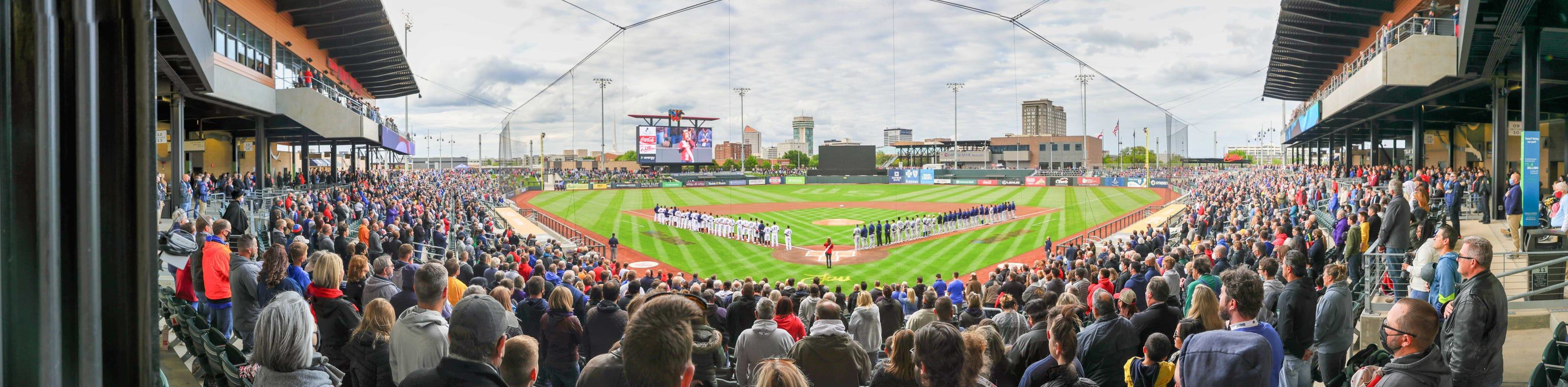 A panoramic view across a full ballpark toward the Wichita skyline, with both teams lined up along the baselines